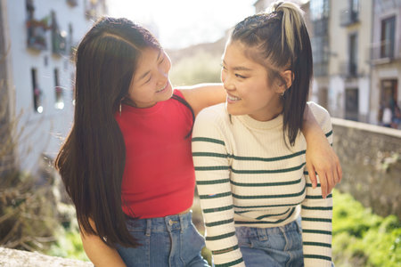 Happy Asian woman sitting with hand on shoulder of friend while looking at each other against blurred background in Granadaの写真素材