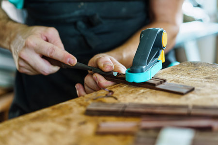 Soft focus of unrecognizable craftsman carving part for Spanish flamenco guitar on workbench during work in luthier workshopの写真素材