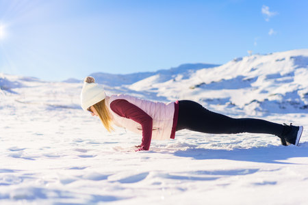 Side view of focused young female in warm clothes and sunglasses, lying in Chaturanga yoga pose on...