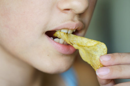 Closeup of crop anonymous young girl biting crunchy potato chip at homeの写真素材