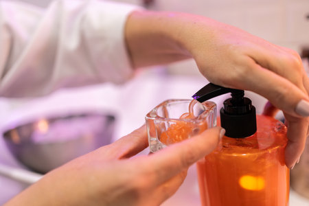 Crop female in white clothes dispensing cream in glass jar during cosmetic session in beauty salonの写真素材
