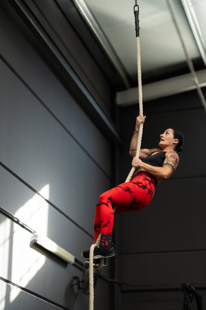 Vertical photo of a strong woman climbing rope in a cross training gymの写真素材