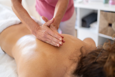 Crop anonymous female osteopath kneading back of patient with special technique during massage session in modern rehabilitation clinicの写真素材