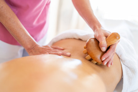 From above of crop anonymous massage therapist massaging with wooden therapy tool back of client lying on table during osteopathy session in clinicの写真素材
