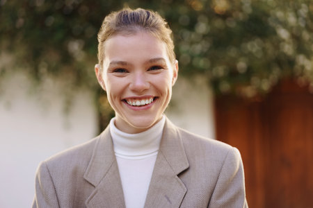 A smiling and cheerful young woman wearing a trendy stylish blazer paired with a fashionable...