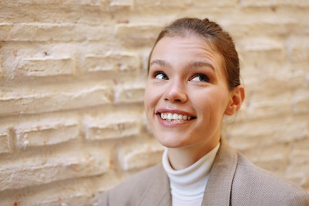 A joyful young woman, radiating happiness with her bright and warm smile, is beautifully captured in a candid moment against a rugged, textured stone wall that adds depth to the sceneの写真素材