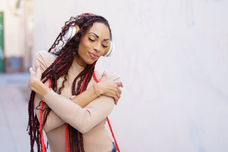 In a lively urban environment, a joyful woman with long, beautiful braids listens to her favorite...
