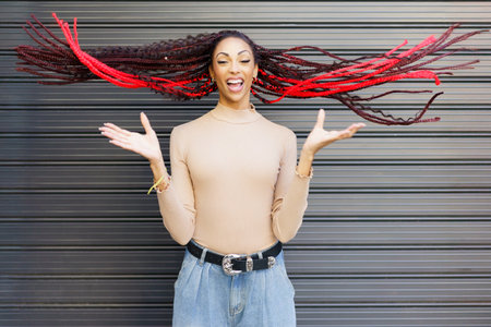 A vibrant woman with bold red and black braided hair exudes excitement. Her playful pose and stylish...