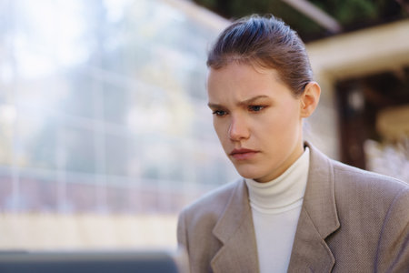 A young woman dressed in a contemporary and stylish outfit stands alone in a bustling urban environment while appearing pensive, lost in her deep thoughts amid a calm and serene backdropの写真素材