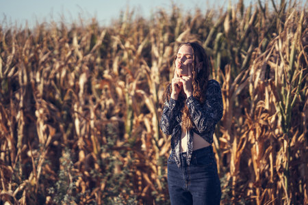 In a vast and vibrant cornfield, a young woman stands amidst towering stalks, savoring a delightful moment of peace and connection with nature, radiating a genuine sense of happiness and tranquilityの写真素材