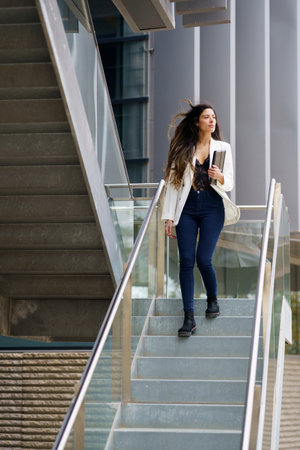 A chic and stylish young woman gracefully descends a modern staircase, demonstrating both the...