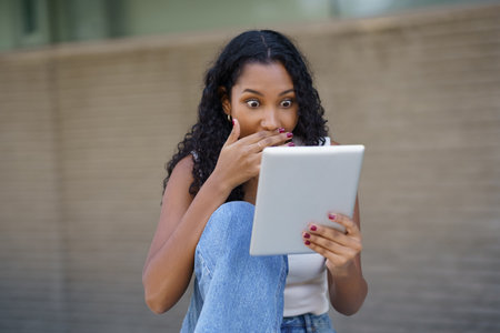 A young woman displays a reaction of surprise while using her tablet, capturing a delightful moment of joy and active engagement in a laidback outdoor setting surrounded by natureの写真素材