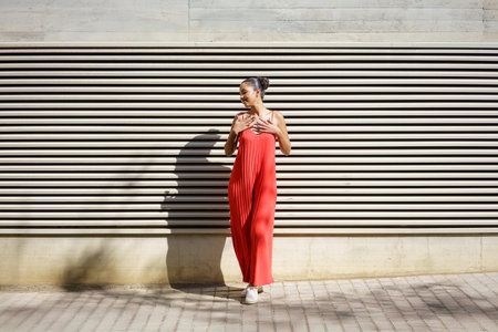 A stylish and fashionable woman poses confidently in a vibrant and eyecatching red dress, standing proudly against a modern textured wall, showcasing her contemporary style and elegant personalityの写真素材