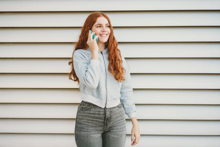 A cheerful and happy young woman with long, curly hair is engaged in an animated phone conversation...