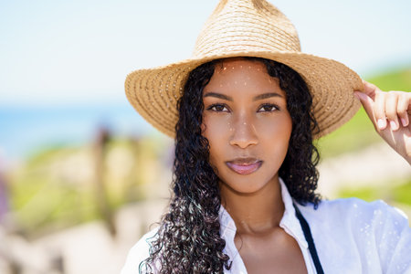 A young woman joyfully wears a charming straw hat and stylish white shirt at the beach, radiating cheerful summer energy that captivates everyone nearby, creating a memorable scene of summer beautyの写真素材