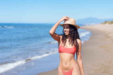 A beautiful woman radiates joy on a sunny beach, wearing a stylish bikini and an elegant sun hat. This scene captures the essence of fun and relaxation, perfect for summerthemed projectsの写真素材