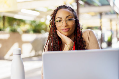 In a lively and vibrant outdoor setting, a woman sits comfortably in a charming cafe, deeply focused as she engages with her laptop, reflecting on her ideas and enjoying the ambiance around herの写真素材