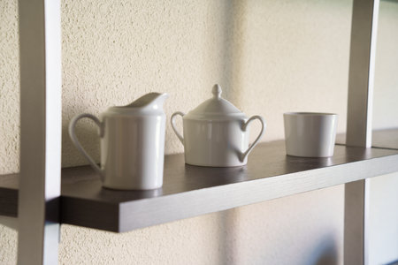 Creamer and sugar bowl arranged peacefully in morning glow, Stylish ceramic items displayed on shelf with calming light and textured backgroundの写真素材