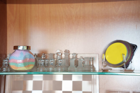 Glass shelf with sand jar and small clear bottles, yellow compact mirror, warm wood backing, soft...