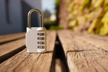 Combination padlock on wooden bench, sunlit close-up with shallow depth of field and warm bokeh background. Focus on textured metal and weathered wood. Sceneの写真素材