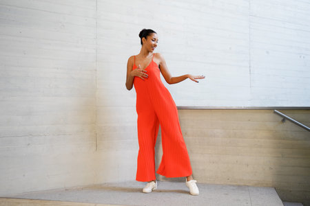 Woman in orange jumpsuit gesturing playfully midmotion, expressive hand and relaxed sneakers set...