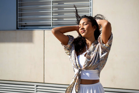 Goldenhour outdoor selfcare portrait woman basking, eyes closed and hands resting behind head, soft smile with sunlit skin and textured blouse, modern urbanの写真素材
