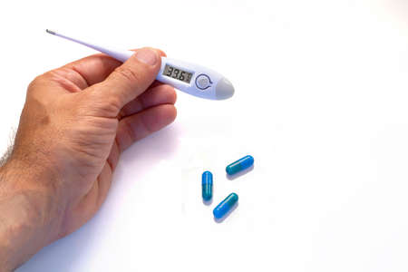 hand with a digital thermometer showing fever values and blue pills on a white background