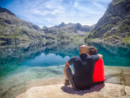 middle aged couple sitting in front of a glacial lake with mountains in the backgroundの写真素材