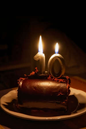 golden birthday candles with the number ten on a chocolate cake, glowing in the dark