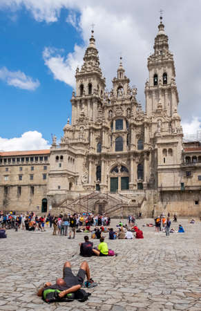 Pilgrim lying down observes the frontage of the Cathedral of Santiago de Compostela, tourists and other pilgrims in the background, Plaza del Obradoiro, Santiago de Compostela, Galicia, verticalのeditorial素材