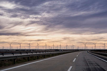 lonely highway at sunrise with a line of windmills on the horizon and soft orange and blue clouds