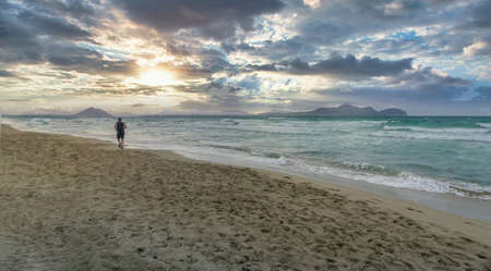 man running on a lonely beach at sunset on a cloudy day, Playa de Muro, Palma de Mallorca, Balearic Islands, Spain, panoramic formatの写真素材