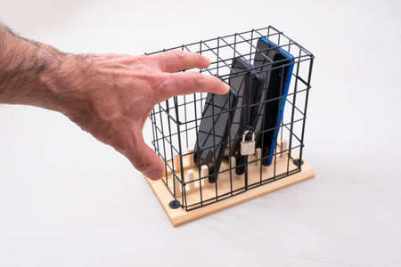 hand trying to catch three mobile phones locked in a cage with a padlock, concept of social...