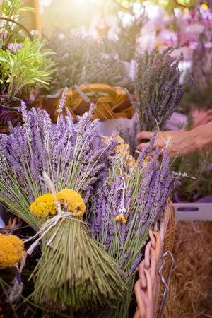 aromatic flower market, a bunch of lavender in a wicker basket in the foreground and an out-of-focus hand holding a bouquet of lavender in the background, verticalの写真素材