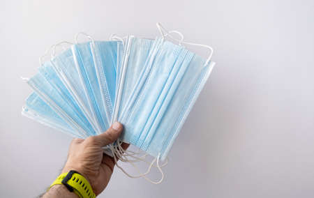 a hand wearing watch with a yellow strap holds a group of surgical face masks on a white background, copy space, horizontalの写真素材