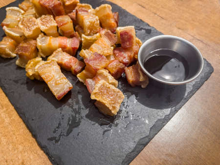 close up of a plate of fried torreznos or fried rashers on a black slate plate and a jar with...