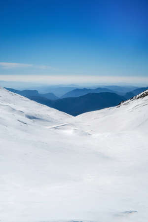 snowy landscape on the top of a mountain, in the background other mountains melting against the horizon with a clear sky, verticalの写真素材