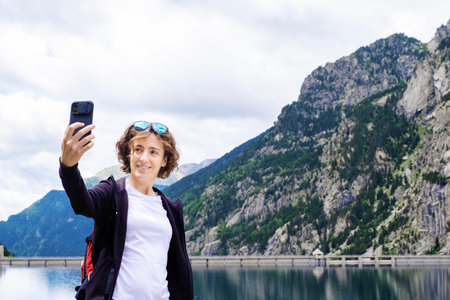 young adult woman taking a selfie in a mountain lake on a day hike, mountains in the background, horizontalの写真素材