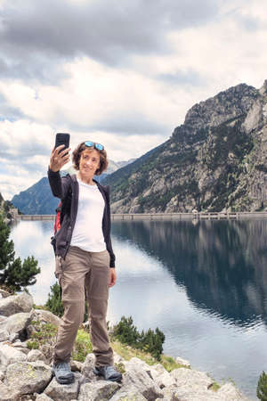 young adult woman taking a selfie in a mountain lake during a trekking day, mountains in the background, verticalの写真素材