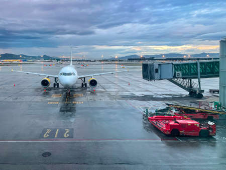 view of an airplane from an airport terminal with a gateway for passengers to enter and a special airport vehicle on a cloudy day with the runway wet from rain, horizontalの写真素材