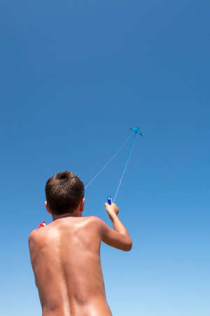 boy on his back playing with a stunt kite seen from below with the kite high up in the blue sky on a summer day, copy space, verticalの写真素材