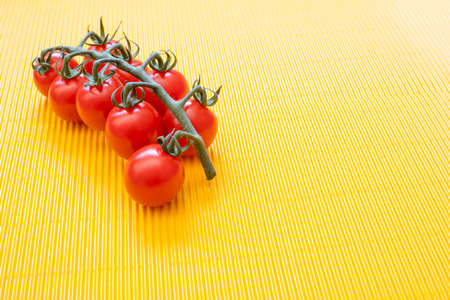 group of vine cherry tomatoes on a yellow wavy background, vegan or vegetarian diet, fresh natural foods, copy spaceの写真素材