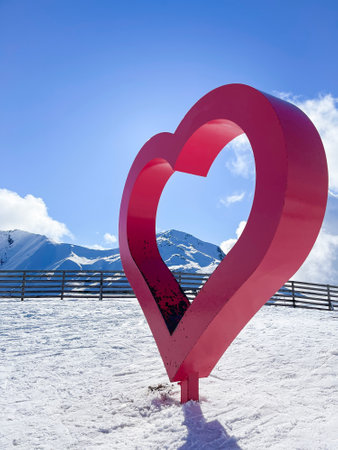a big red metal heart in the middle of a ski slope, with snowy mountains, passion for skiing, winter sport, valentines day, copy space, verticalの写真素材