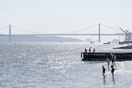 women and children refresh their feet on a summer day at a pier with a dock in Lisbon on the estuary...