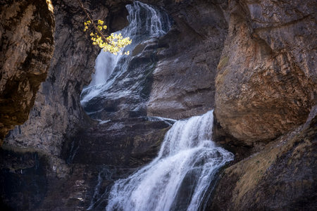 The Cave waterfall in the heart of the National Park of Ordesa and Monte Perdido, set in a rocky canyon, branches with autumn colored leavesの写真素材