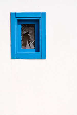 a small window with a blue wooden frame with a broken glass, on a white facade, verticalの写真素材