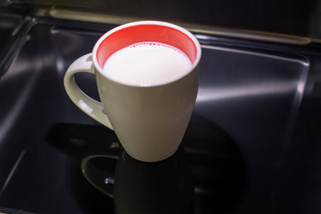 a white milk mug with a red interior inside a stainless steel microwave, a cup of milk heating up in the kitchen microwave, horizontalの写真素材