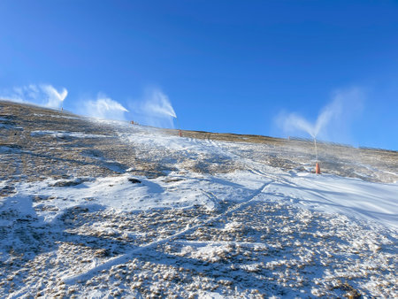 a ski slope without snow being snowed with artificial snow with snow cannons, the problem of the lack of snow in the ski resorts, horizontalの写真素材