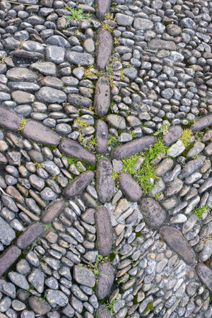 detail of a cobblestone street with rounded stones, decorated with lines and some weeds growing in the joints, top view, verticalの写真素材