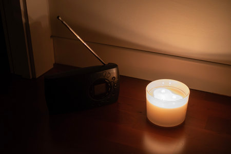 Emergency candlelight and portable radio on the floor during a power outage, symbolizing survival,...